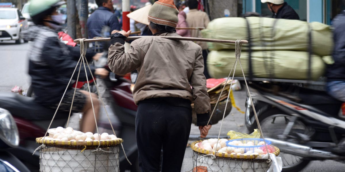 A street vendor crosses a busy avenue in Hanoi © | Nikki Vargas