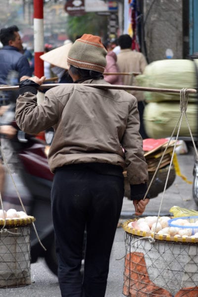 A street vendor crosses a busy avenue in Hanoi © | Nikki Vargas