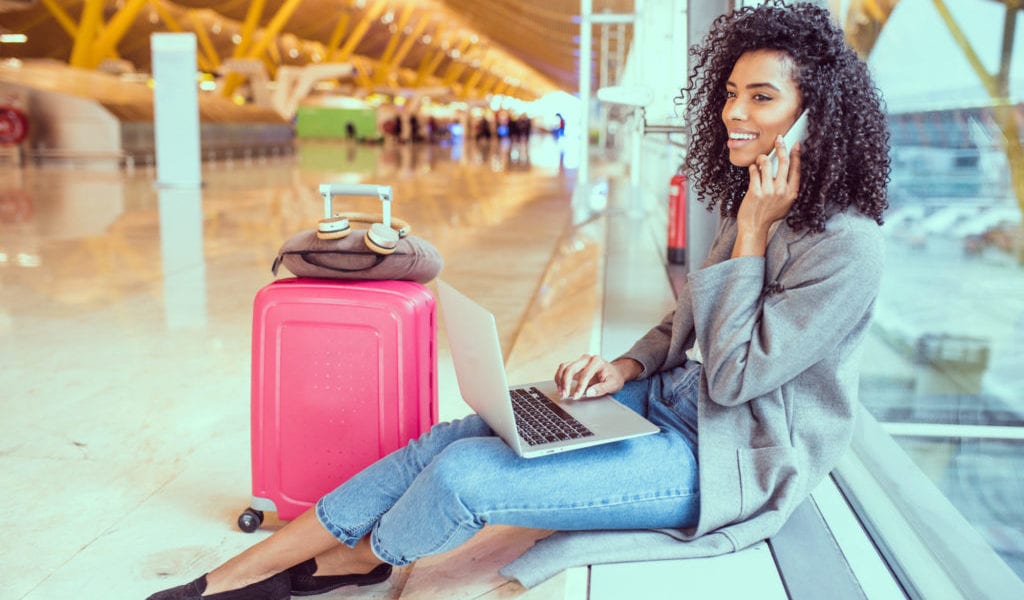 A young woman sits at the airport on her laptop | © David Prado Perucha/Shutterstock