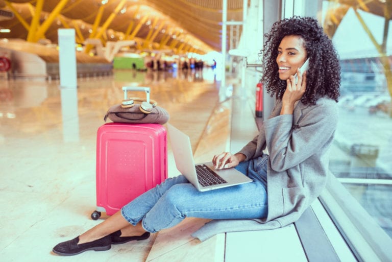 A young woman sits at the airport on her laptop | © David Prado Perucha/Shutterstock