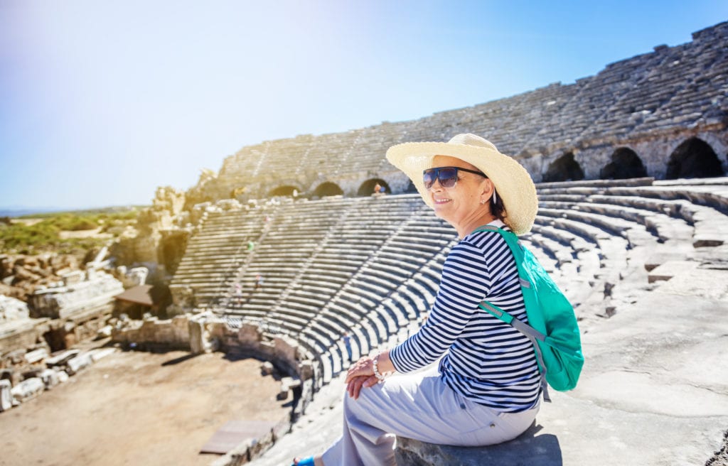 Mature beautiful woman traveler, sits on the steps of the amphitheater in Greece | © Olesya Kuznetsova