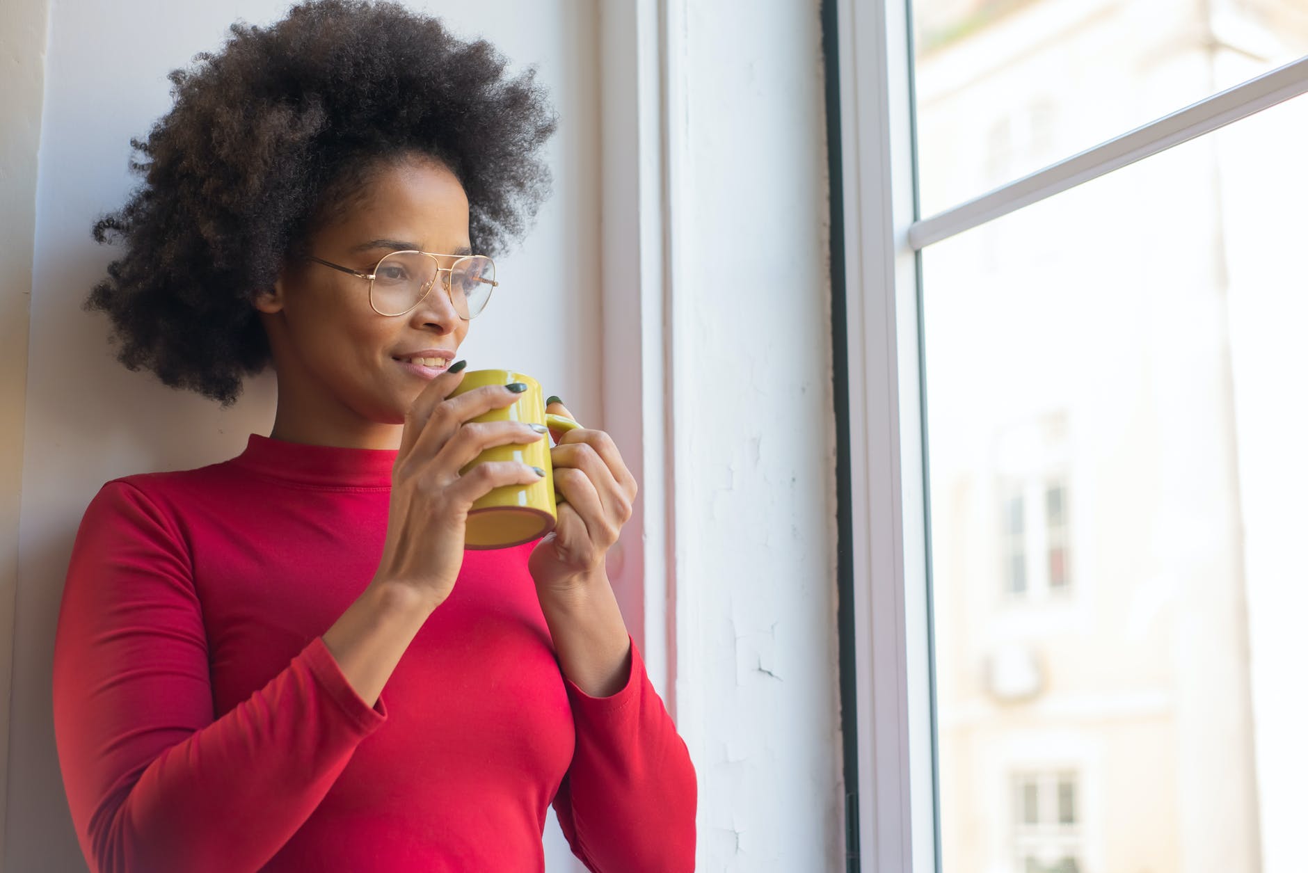 a woman holding a cup while looking out the window