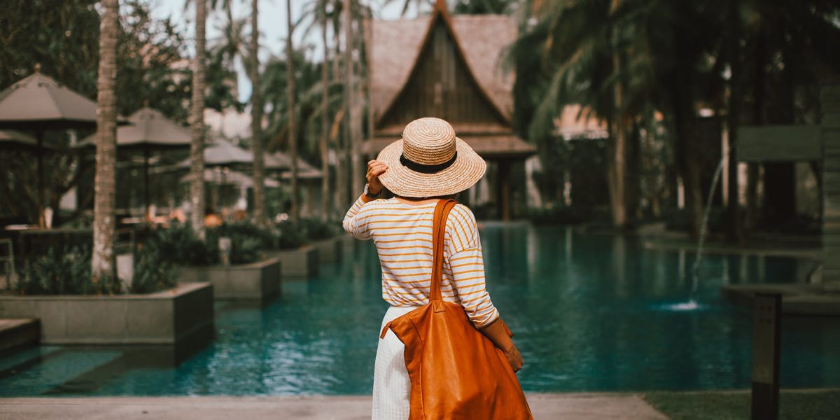 unrecognizable woman in hat standing on poolside in resort