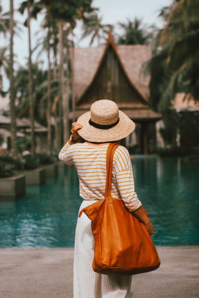 unrecognizable woman in hat standing on poolside in resort